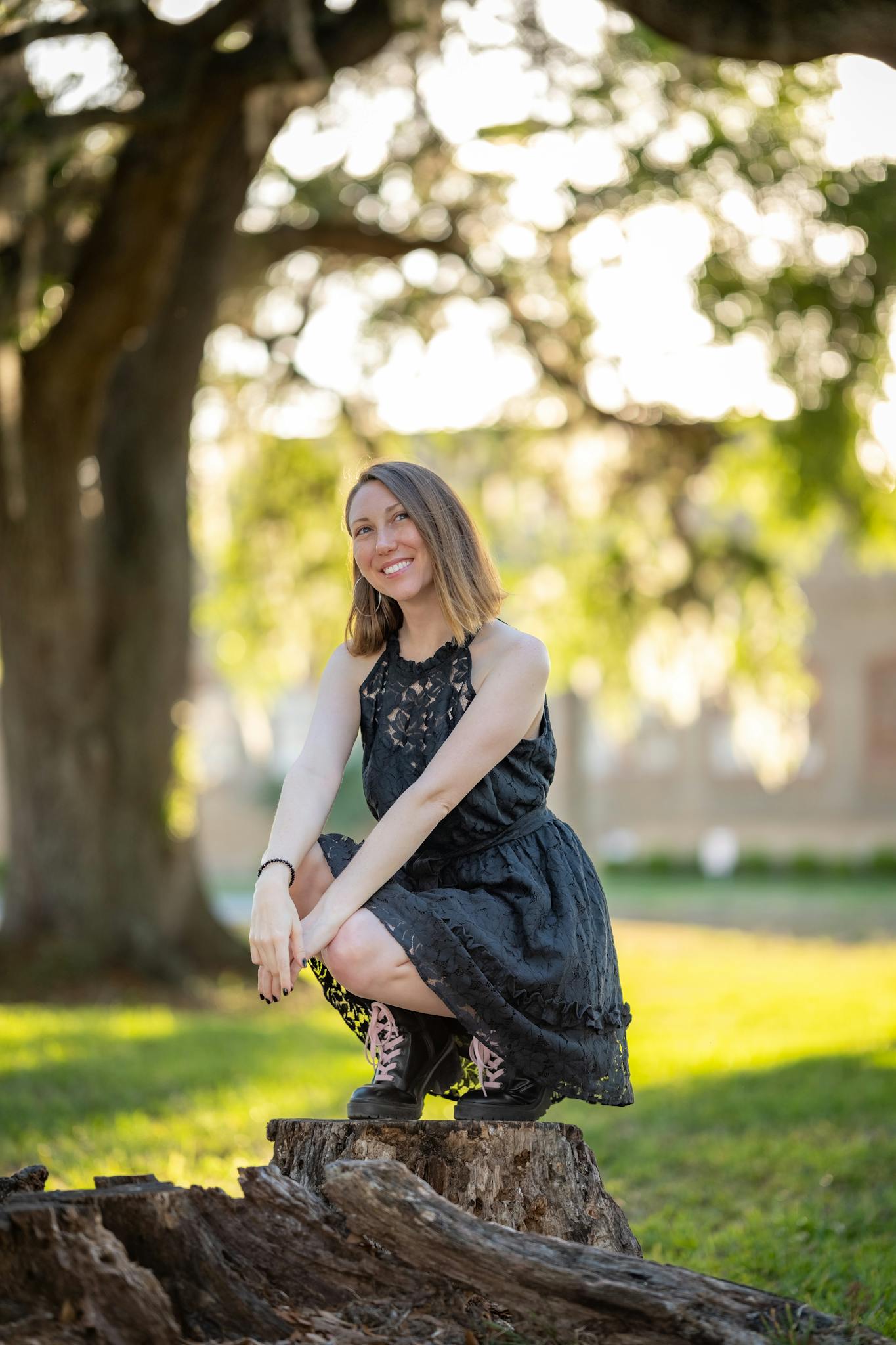 A young woman in a black dress sits on a stump